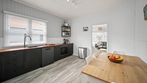 A modern kitchen with grey cabinets, a wooden countertop, and a dining area with a wooden table and chairs. - Summer Breeze Forster
The Perfect Family Getaway on the Mid North Coast of NSW (Forster)