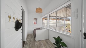 A hallway with white walls, a wooden floor, a potted plant, a door, and a window with blinds. - Summer Breeze Forster
The Perfect Family Getaway on the Mid North Coast of NSW (Forster)