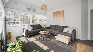 A modern living room with a sectional sofa, a round coffee table, and a large window with blinds. - Summer Breeze Forster
The Perfect Family Getaway on the Mid North Coast of NSW (Forster)
