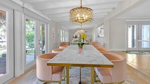 A dining area with a marble table, pink chairs, and a chandelier. - Flirty Flamingo: Colorful Waterfront Escape w/ Pool (Wilton Manors)