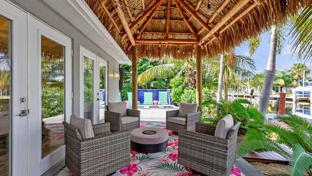A covered outdoor seating area with wicker furniture and a tropical-themed floor mat. - Flirty Flamingo: Colorful Waterfront Escape w/ Pool (Wilton Manors)