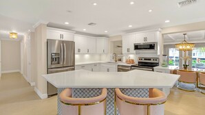 A modern kitchen with white cabinetry, stainless steel appliances, and a central island with bar stools. - Flirty Flamingo: Colorful Waterfront Escape w/ Pool (Wilton Manors)