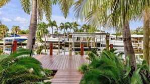 A wooden dock leading to a marina with boats and palm trees. - Flirty Flamingo: Colorful Waterfront Escape w/ Pool (Wilton Manors)