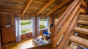 A wooden interior with a staircase, a leather sofa, and a view of the outside.