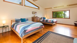 A bedroom with two beds, a dresser, a mirror, and a window with a view of trees.