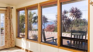 Una habitación con ventanas amplias, vistas a palmeras y una banca afuera.