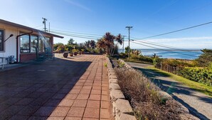 Una proprietà vista mare con vialetto in pietra che conduce a un patio coperto e un giardino curato con diverse piante.