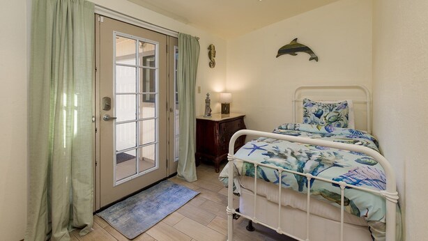 Un dormitorio con una cama, una mesita de noche, una lámpara, un adorno en la pared y una puerta con cortinas.