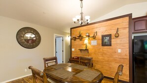 A dining area with a wooden table and chairs, a chandelier, and a refrigerator.