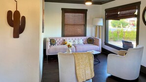 Ein Wohnzimmer mit einer Couch, zwei Sesseln, einer Kakteen-Dekoration, einem Deckenventilator und einem Fenster mit Jalousien.