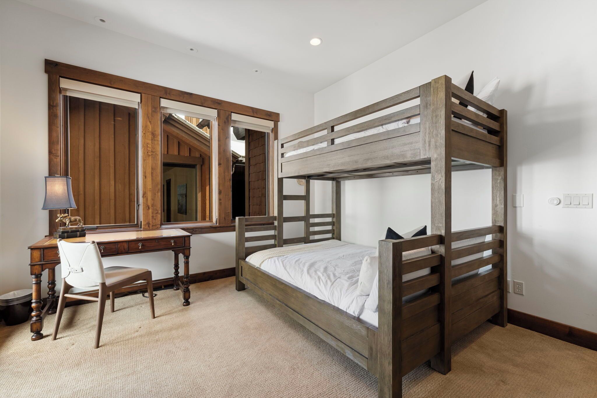 A bunk bed with a wooden frame, a desk with a chair, and a mirror.