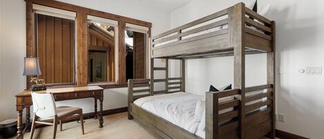 A bunk bed with a wooden frame, a desk with a chair, and a mirror.