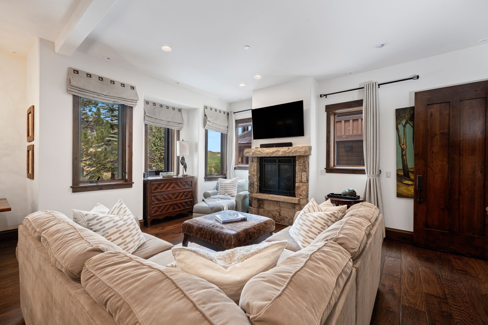 A spacious living room with a fireplace, large windows, and a flat-screen TV mounted on the wall.