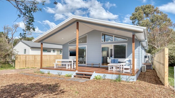 A modern two-story house with a covered patio, large windows, and a wooden deck.
