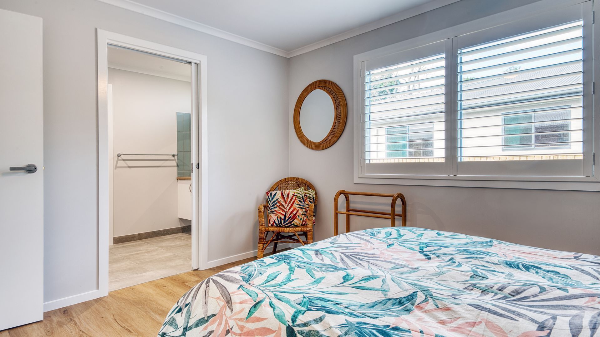 A bedroom with a bed, a chair, a window with blinds, a mirror, and a door leading to another room.