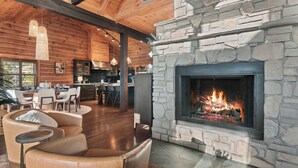 Una sala de estar acogedora con chimenea de piedra, sofá de cuero, comedor y cocina al fondo.