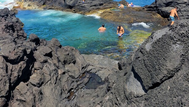 A rocky coastal area with clear blue water and people swimming and relaxing on the rocks.