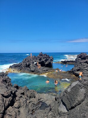 A rocky coastal area with clear blue water and people swimming and relaxing on the rocks.