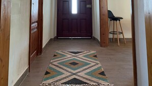 A wooden hallway with a patterned rug, a dark wooden door, and a wall-mounted light fixture.