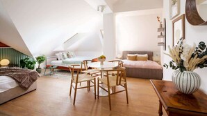 Ein modernes Schlafzimmer im Loft-Stil mit schrägem Dach, einem runden Esstisch mit Stühlen, einem Bett mit grünem Kopfteil und einem Nachttisch mit Blumenvase.