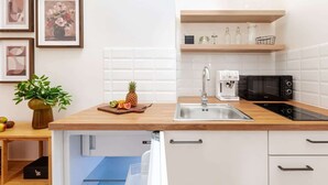 Eine moderne Küche mit weißen Schränken, einer Holz Arbeitsplatte, einer Spüle, einer Mikrowelle und einem eingebauten Backofen. An der Wand hängen Bilder in Rahmen und auf der Arbeitsplatte steht eine Pflanze.