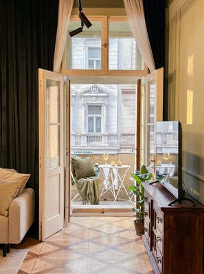 Una habitación con un gran ventanal que da a un balcón con mesa, sillas y vistas a edificios.