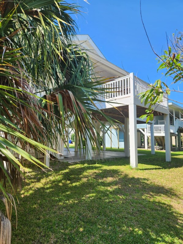A covered outdoor area with a white structure, palm trees, and a clear blue sky.