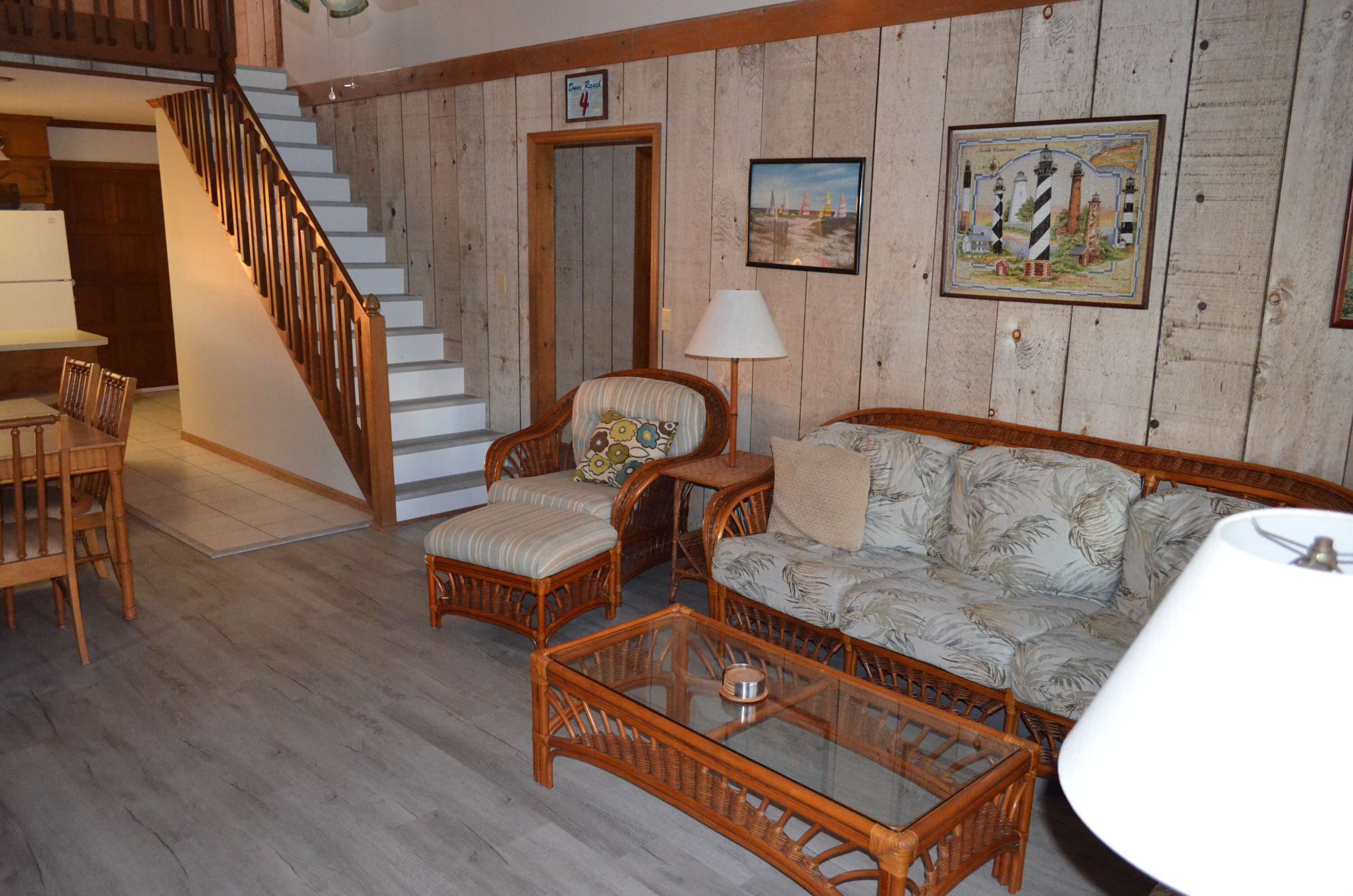A wooden-floored living room with wicker furniture, a staircase, and a framed picture on the wall.