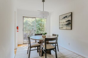 Un coin repas avec une table ronde, quatre chaises, un luminaire suspendu, un extincteur et une fenêtre donnant sur un paysage verdoyant.