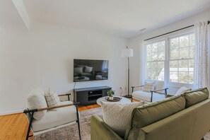 Un salon moderne avec un téléviseur à écran plat, un canapé, un fauteuil et une lampe sur pied.