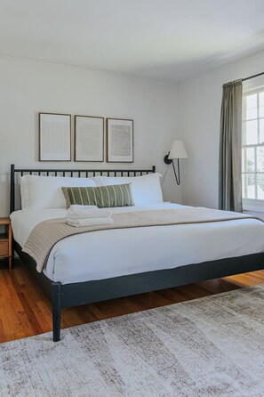 Une chambre à coucher avec un lit, une table de chevet, une lampe et une fenêtre avec des rideaux.