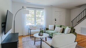 A living room with a green sofa, white armchairs, a coffee table, and a TV on a black stand.