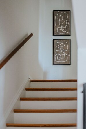 A staircase with wooden steps and a handrail, leading to a landing with two framed abstract artworks.