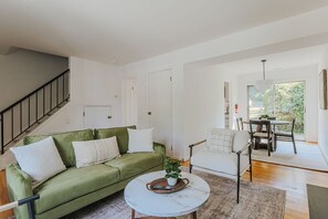 Un salon moderne avec un canapé vert, un fauteuil blanc, une table basse ronde et un coin repas comprenant une table et des chaises.