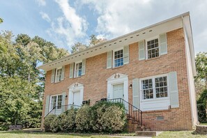 A two-story brick building with white shutters, a front porch, and a staircase leading to the entrance. - Westerly Haven B: Long term lease available (Charlottesville)