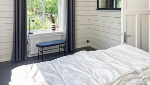 Une chambre à coucher avec un lit, une fenêtre avec des rideaux, un radiateur et un banc.