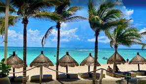 A beach with thatched umbrellas and palm trees, a clear blue sky, and the ocean. - Vacation Mode Casa 
The townhome with an easy vibe
 (Akumal)