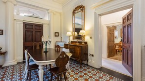 Comedor con una mesa grande, sillas y un espejo. Se ve una puerta que da a otra habitación.