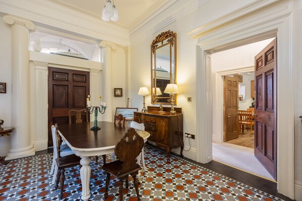 Une salle à manger avec une grande table, des chaises et un miroir. Une porte donne accès à une autre pièce.