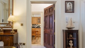 Un pasillo con una puerta de madera, un espejo, una lámpara, un busto y un cuadro enmarcado en la pared.