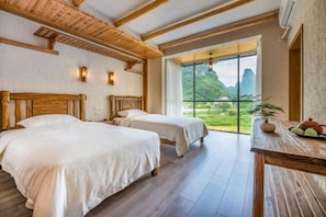 Een kamer met twee bedden, een houten plafond en een groot raam met uitzicht op groen.