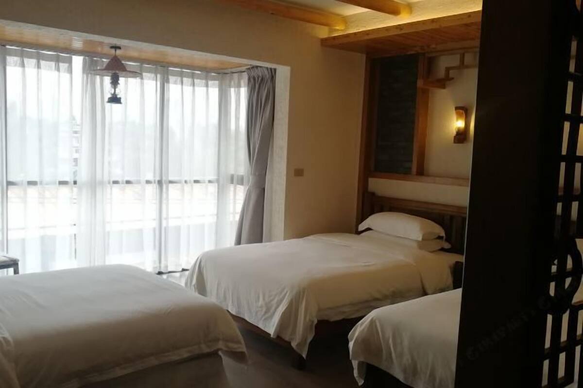 Habitació d'hotel amb dos llits, sostre de fusta, finestra amb cortines i aplíc de paret.