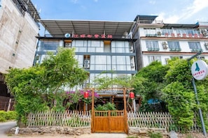 Een hotel in traditionele Chinese bouwstijl, met een houten poort, een witte picket fence en weelderige begroeiing.