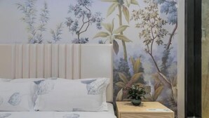 Un dormitorio con cama, mesita de noche, planta en maceta y un papel tapiz floral.