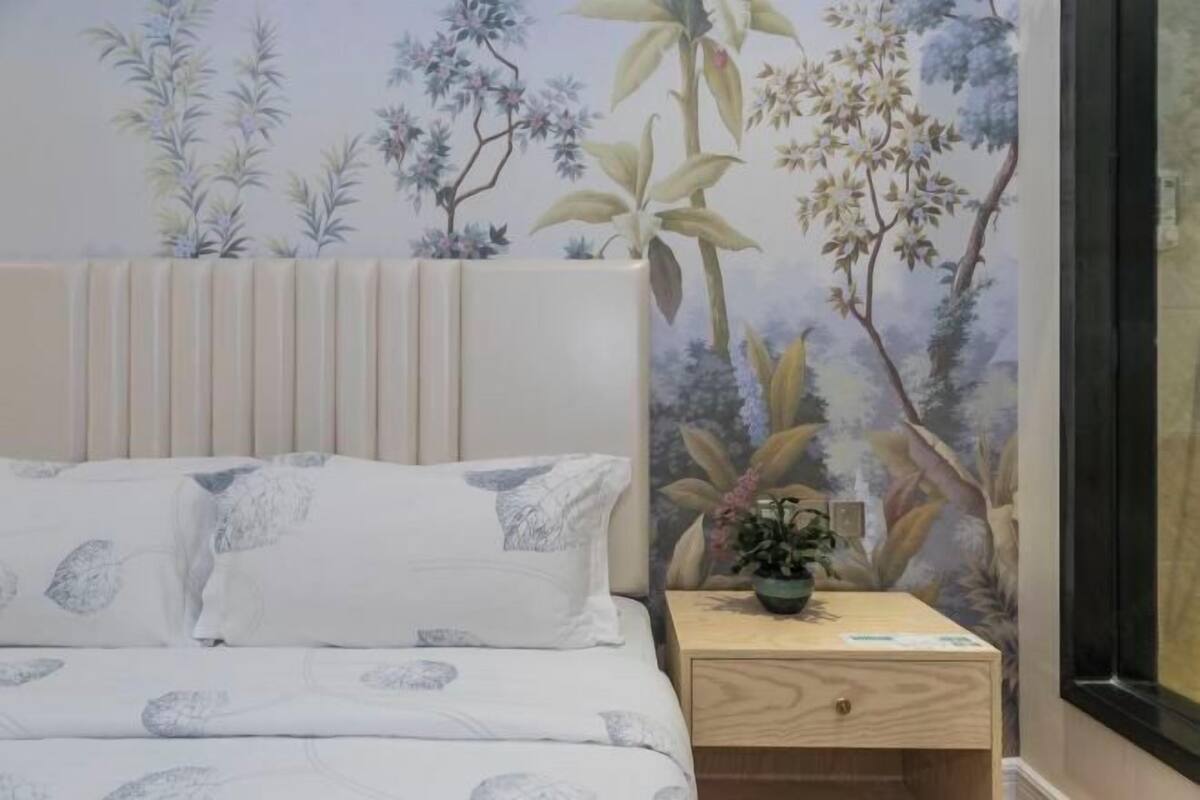 A bedroom with a bed, a nightstand, a potted plant, and a wall with floral wallpaper.