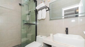 Un baño moderno con cabina de ducha de vidrio, inodoro blanco, lavamanos blanco con grifo negro y un perchero con toallas blancas.