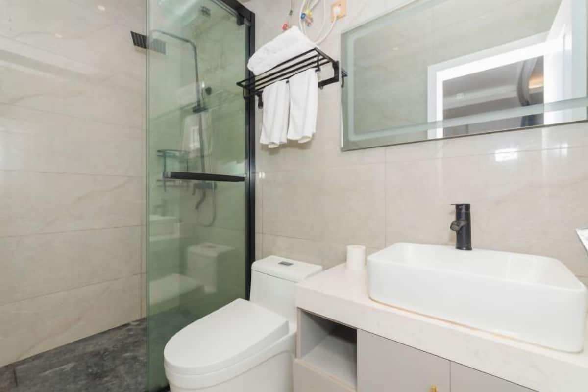 A modern bathroom with a glass shower enclosure, a white toilet, a white sink with a black faucet, and a towel rack with white towels.