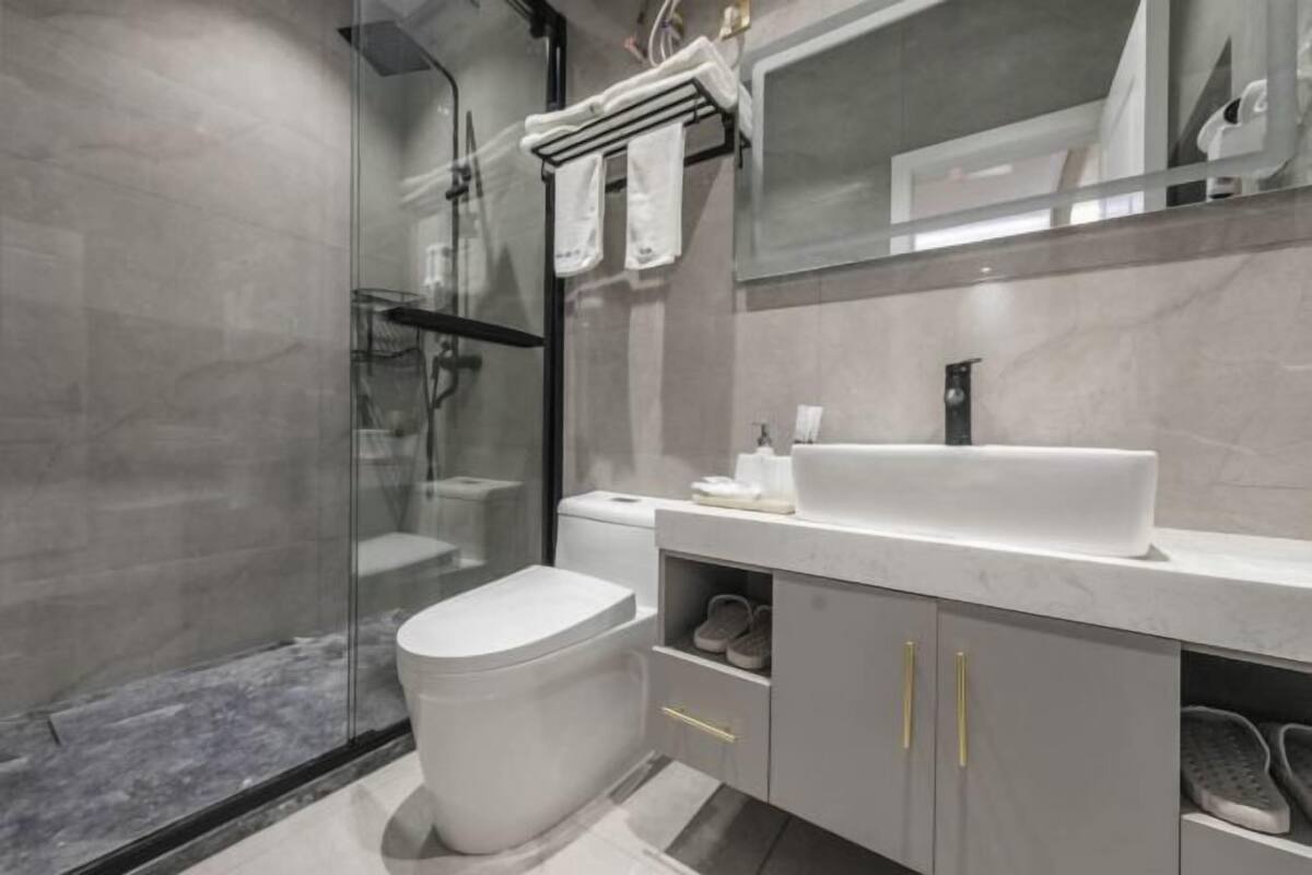 A modern bathroom with a glass shower enclosure, a white toilet, a vanity with a large sink, and a mirror above the sink.