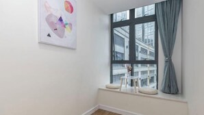 Una habitación con un gran ventanal, una obra de arte abstracta enmarcada en la pared y una pequeña mesa blanca con un cojín.