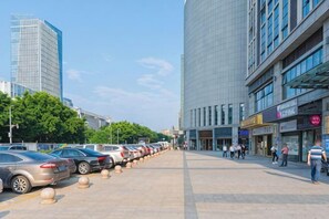 Ein Parkplatz mit Autos, ein Gebäude mit großen Fenstern und Fußgänger auf dem Bürgersteig.